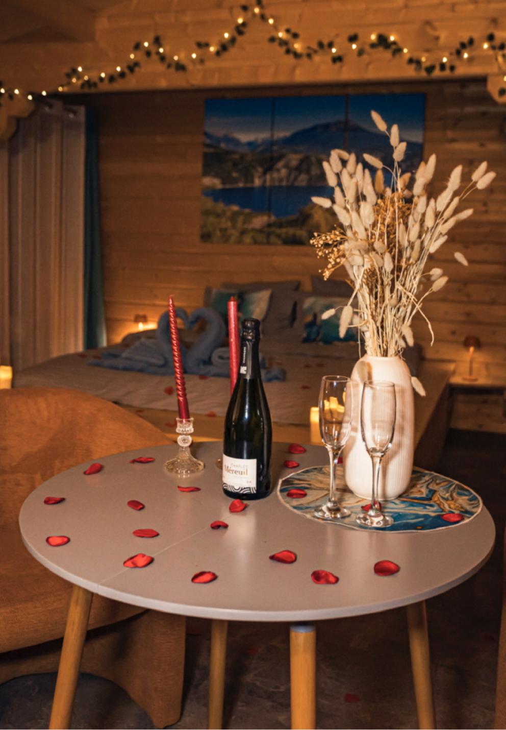 photo de prestation romantique des Lodges de Valière : pétales de roses, bouteille et 2 verres, bouquet de fleurs